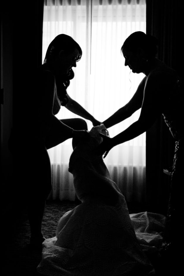 Bridesmaid helping bride get dressed on wedding day