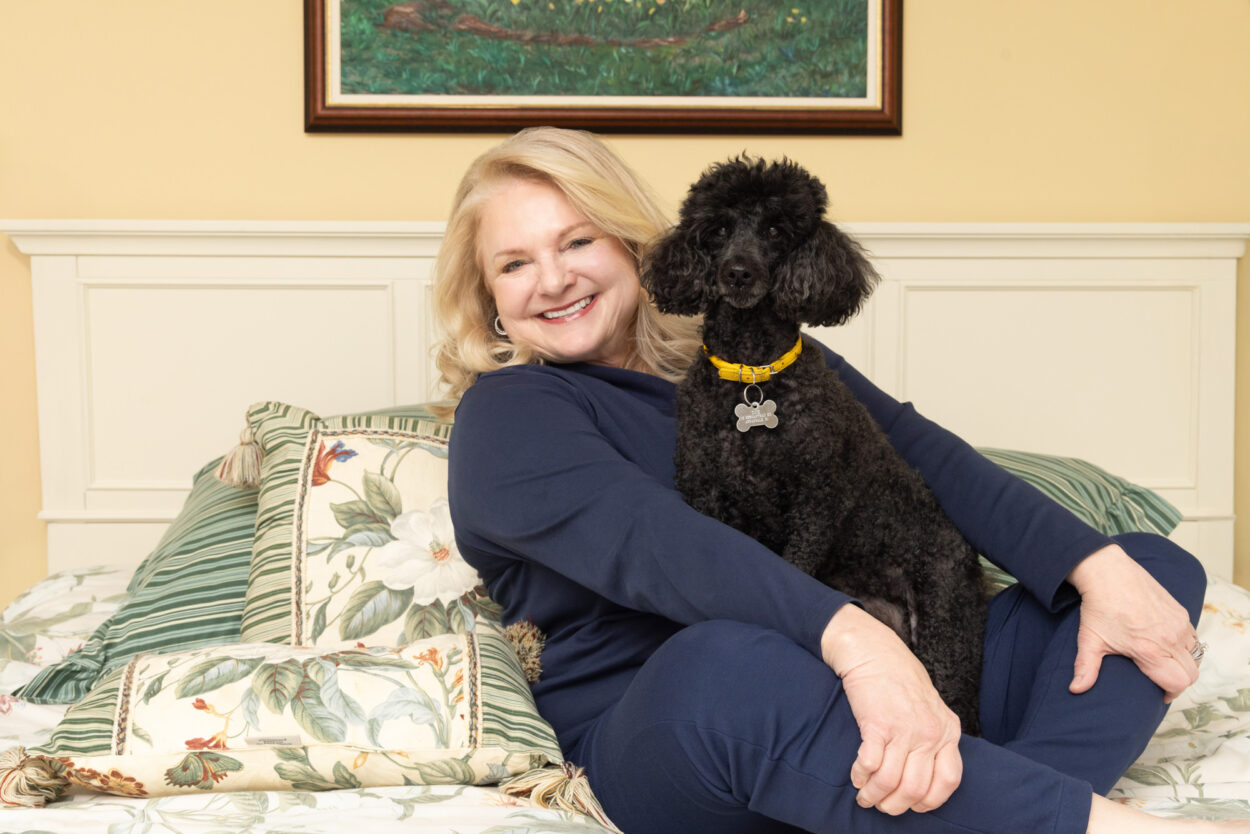 Beautiful blond woman holding her mini poodle in bed during in-home pet photo session in Clinton NJ.
