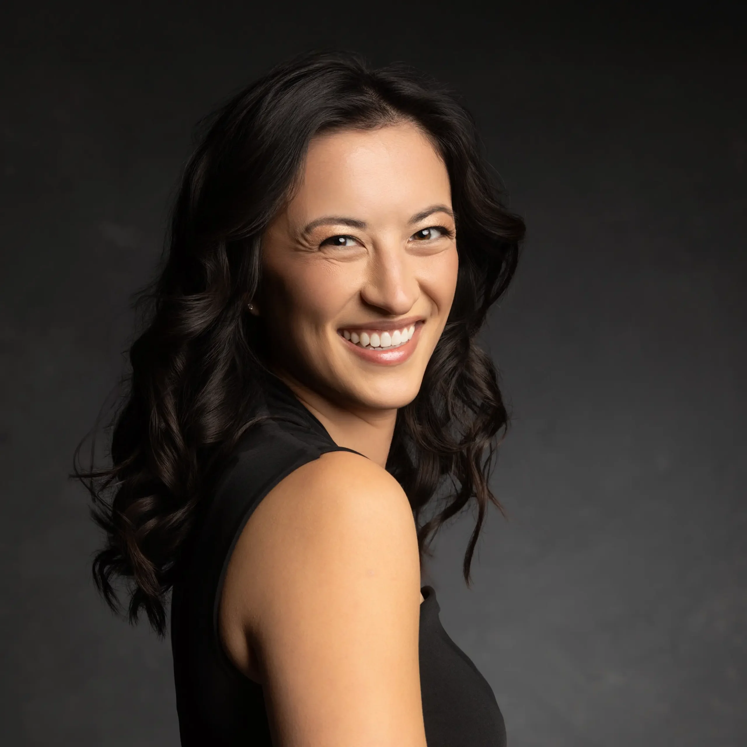 Studio headshot portrait of a woman smiling against a dark background