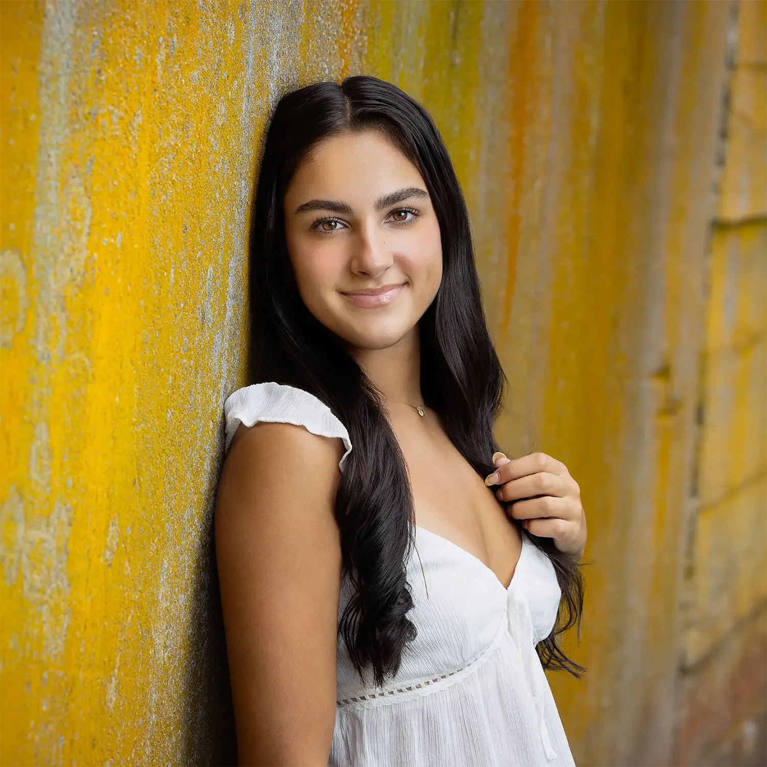 Senior photo of a girl leaning on a yellow wall