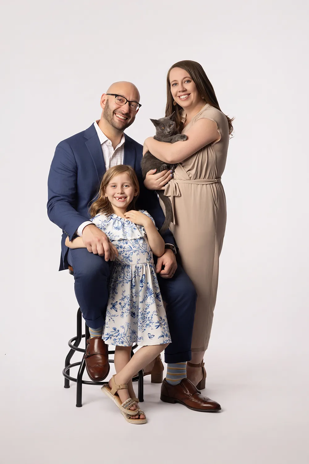 Studio portrait of a young family with a dad, mom, daughter and their cat all smiling against a white background