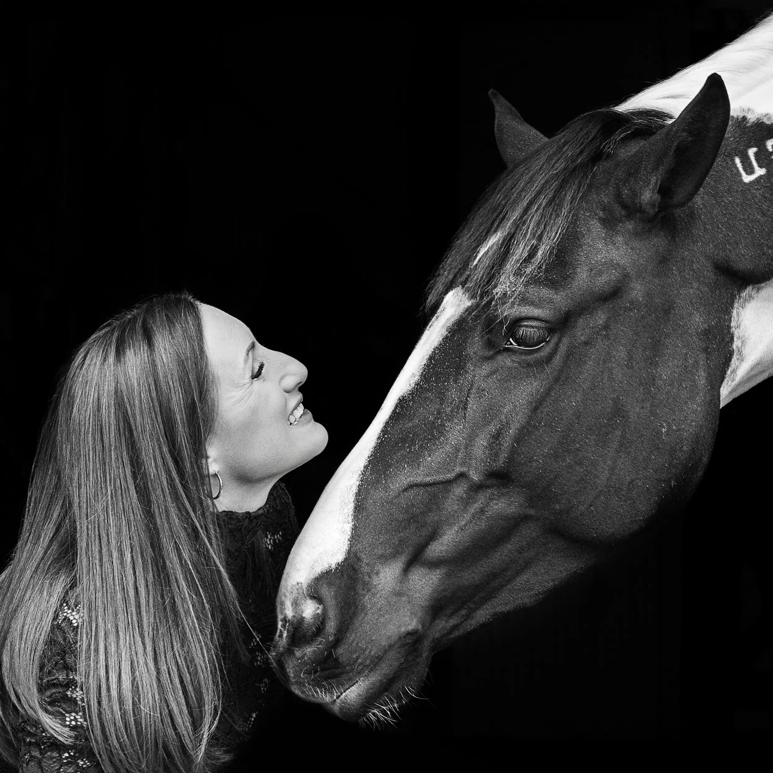 Black and white portrait of a woman standing close to her horse